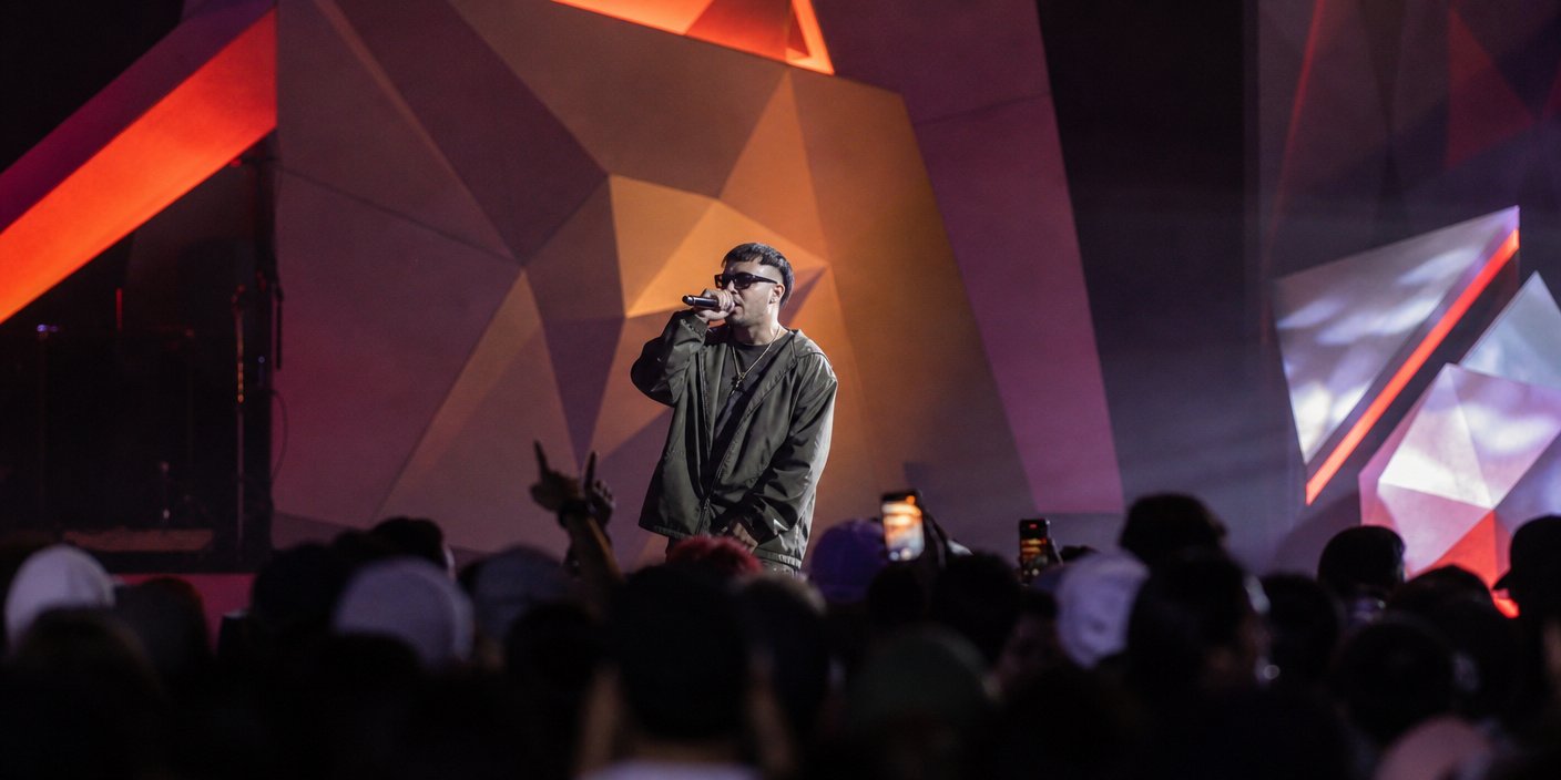 Toyota and Álvaro Díaz Redefining Music Discovery at Lollapalooza | latinmusicnews Male singer wearing a dark jacket performs into a microphone on a stage with bold geometric colorful backdrops crowd visible in the foreground with phones raised